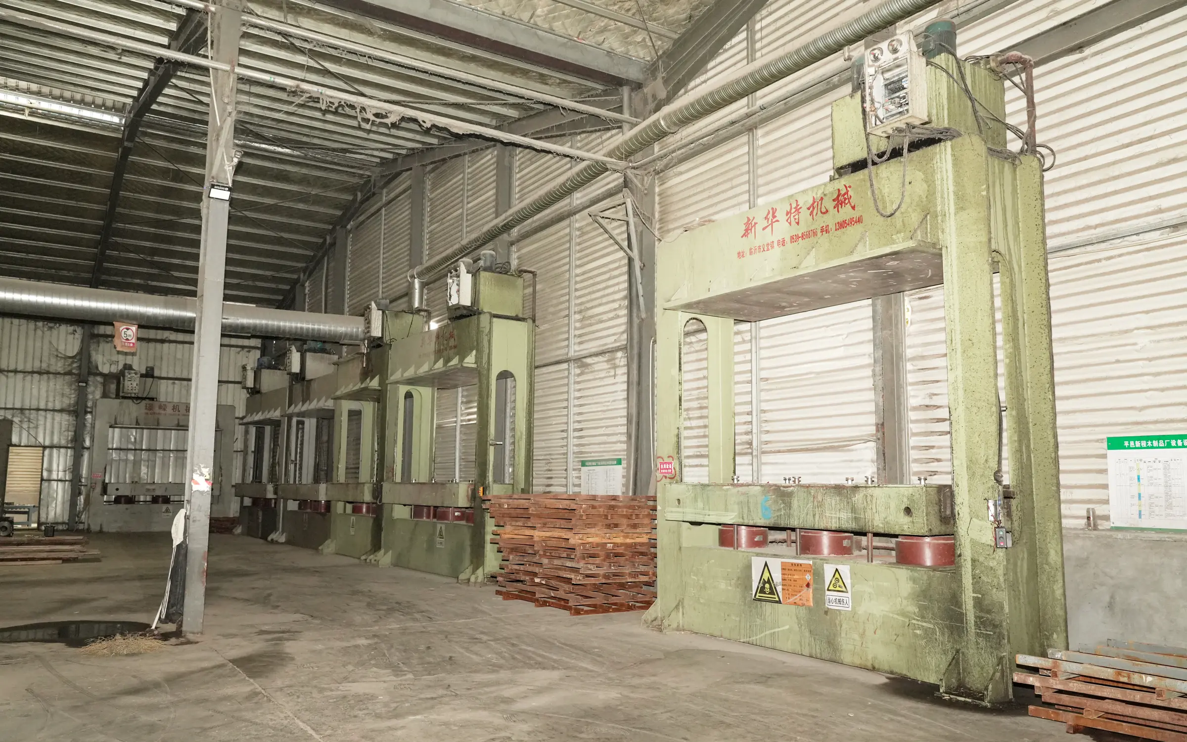 A row of large hydraulic plywood presses inside the factory